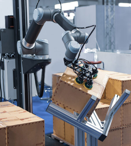 Robot arm handling carton from pallet in modern warehouse.