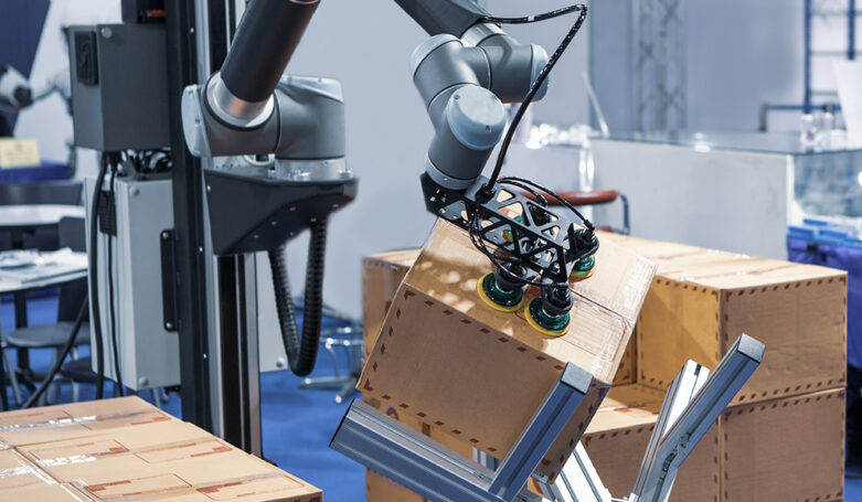 Robot arm handling carton from pallet in modern warehouse.