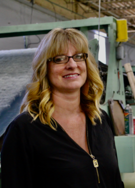 Untitled - May 25, 2026 at 13.39.59-2 A blonde woman with glasses smiling at the camera in a manufacturing setting.