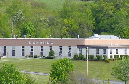 Aerial view of a beige industrial building labeled "Donahue," set amid lush green trees and grass.
