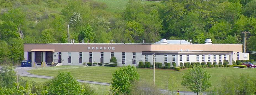 Aerial view of a beige industrial building labeled "Donahue," set amid lush green trees and grass.